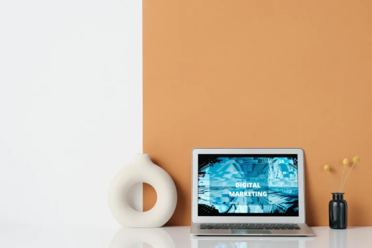 Laptop on a white table against an orange wall background, showcasing a modern workspace setup.