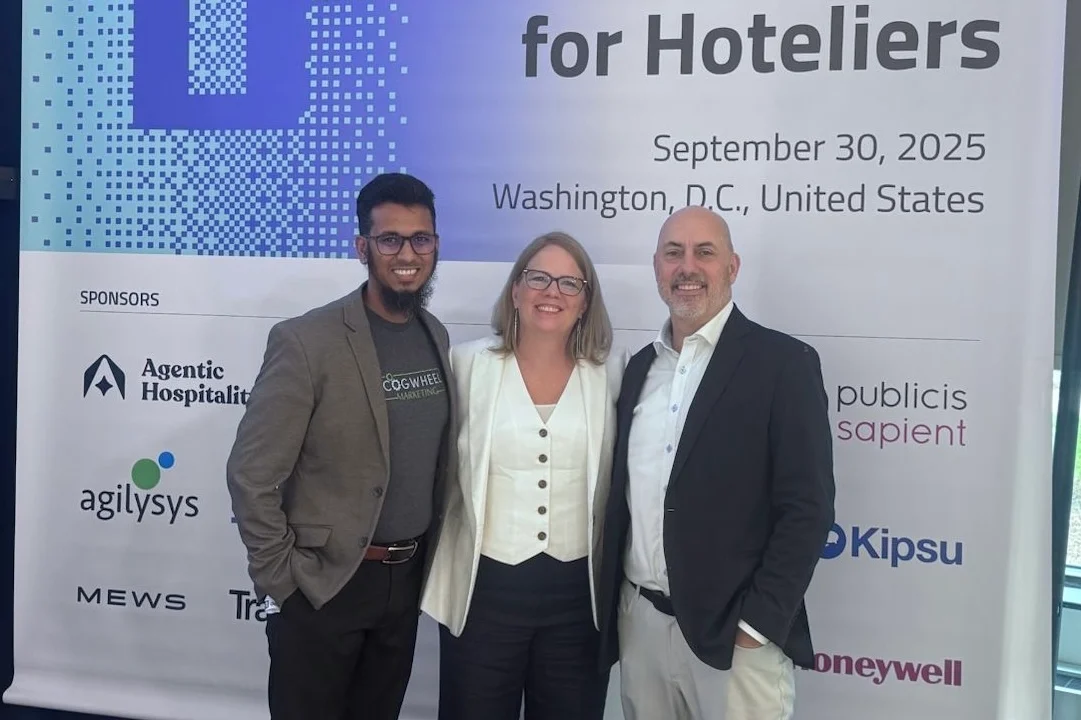 Three attendees pose in front of a banner for "The AI Conference for Hoteliers" in Washington, D.C., showcasing various sponsors.
